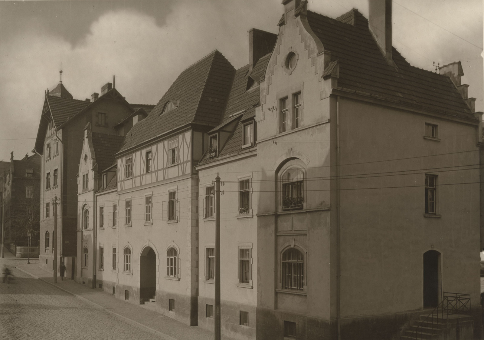 Ein schwarz-weiß Foto zeigt ein mehrstöckiges Gebäude mit Volutengiebel und Fachwerkelementen. Es ist das erste Wohnhaus, das die Jenaer Baugenossenschaft errichtete.