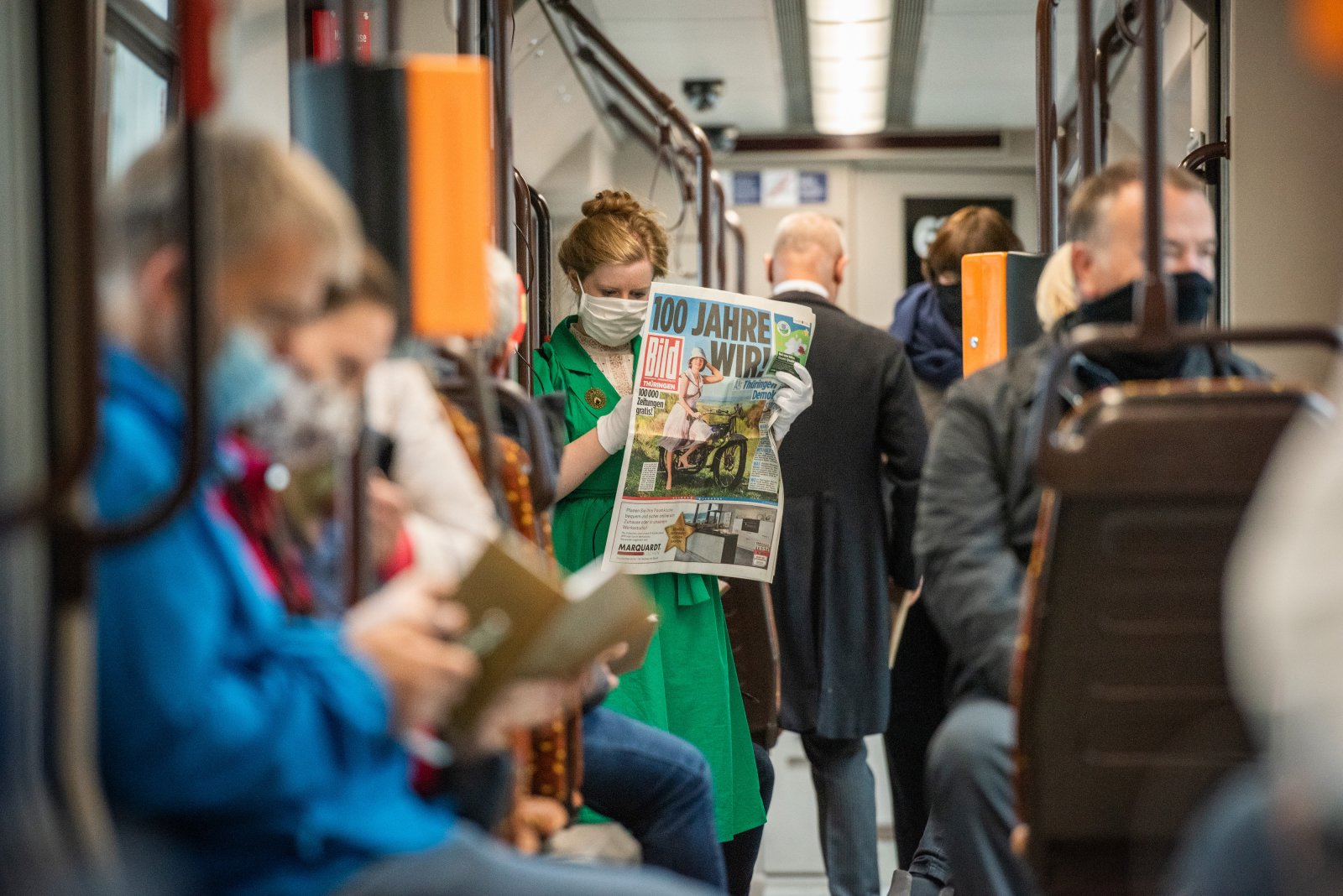 Eine Frau ließt eine Zeitung in der Straßenbahn mit der Schlagzeile "100 Jahre Wir!"